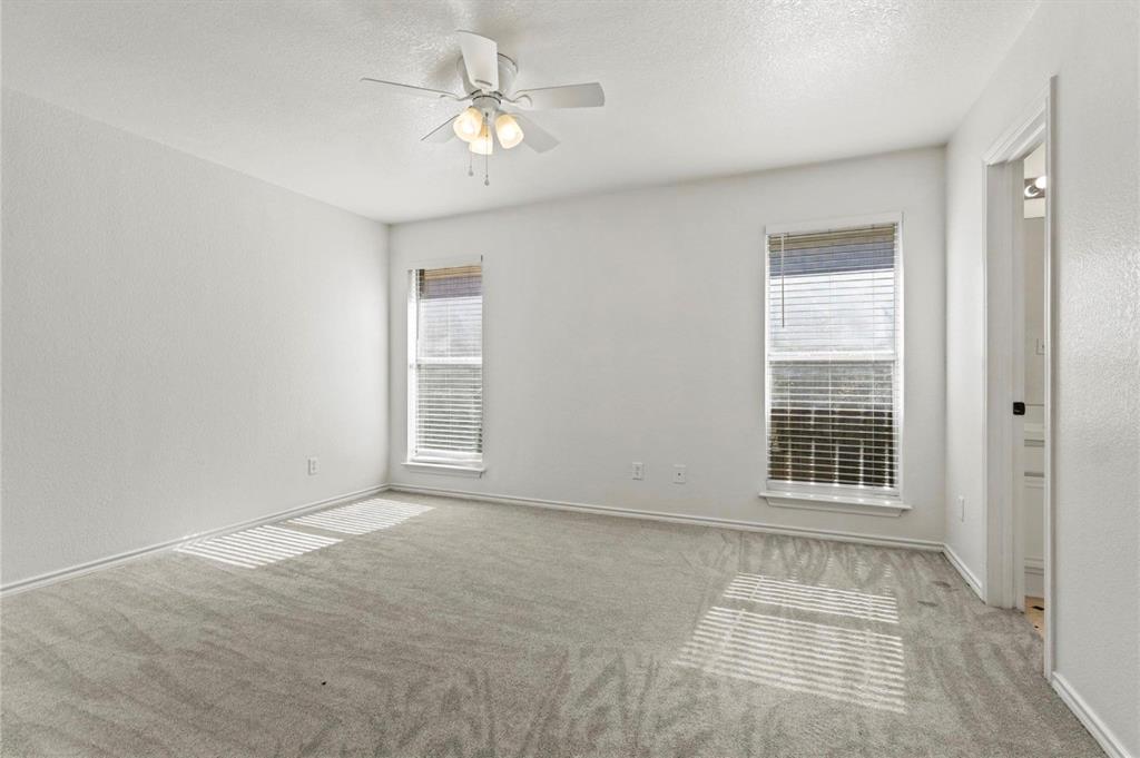 5169 East Rim Road Dallas, TX 75211 - Photo 11 of 19 Bright room featuring two windows with blinds, light gray carpet flooring, a ceiling fan with integrated lighting, and a white interior door frame