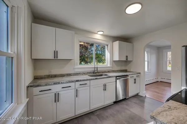 a kitchen with granite countertop a sink stainless steel appliances white cabinets and a window