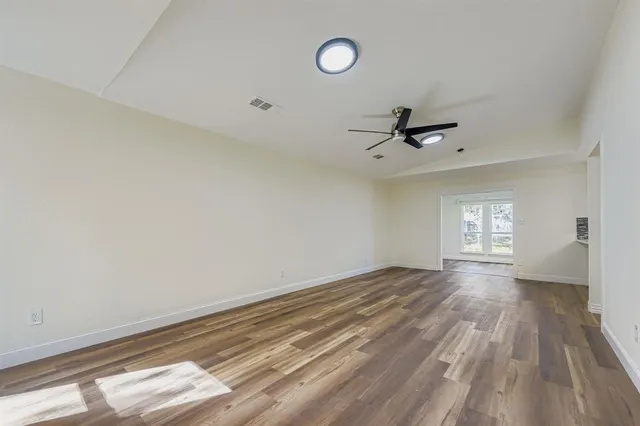 a view of empty room with wooden floor and fan