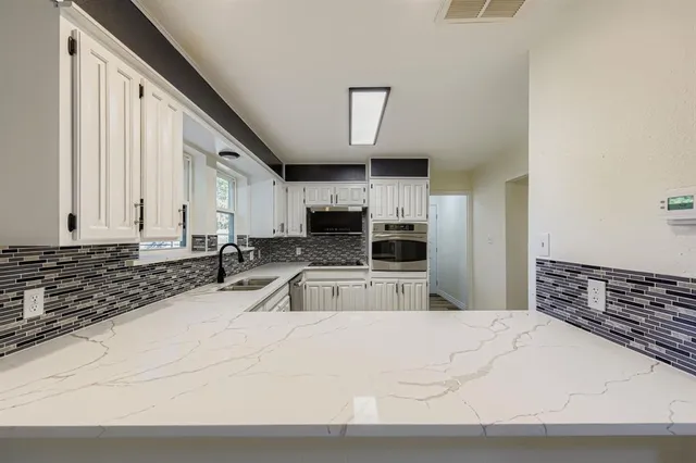 a large white kitchen with stainless steel appliances a sink and a stove