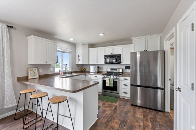 444 South Saddle Road Grantsville, UT 84029 - Photo 5 of 33 Kitchen with stainless steel appliances, a peninsula, a kitchen breakfast bar, white cabinets, and dark wood-style floors