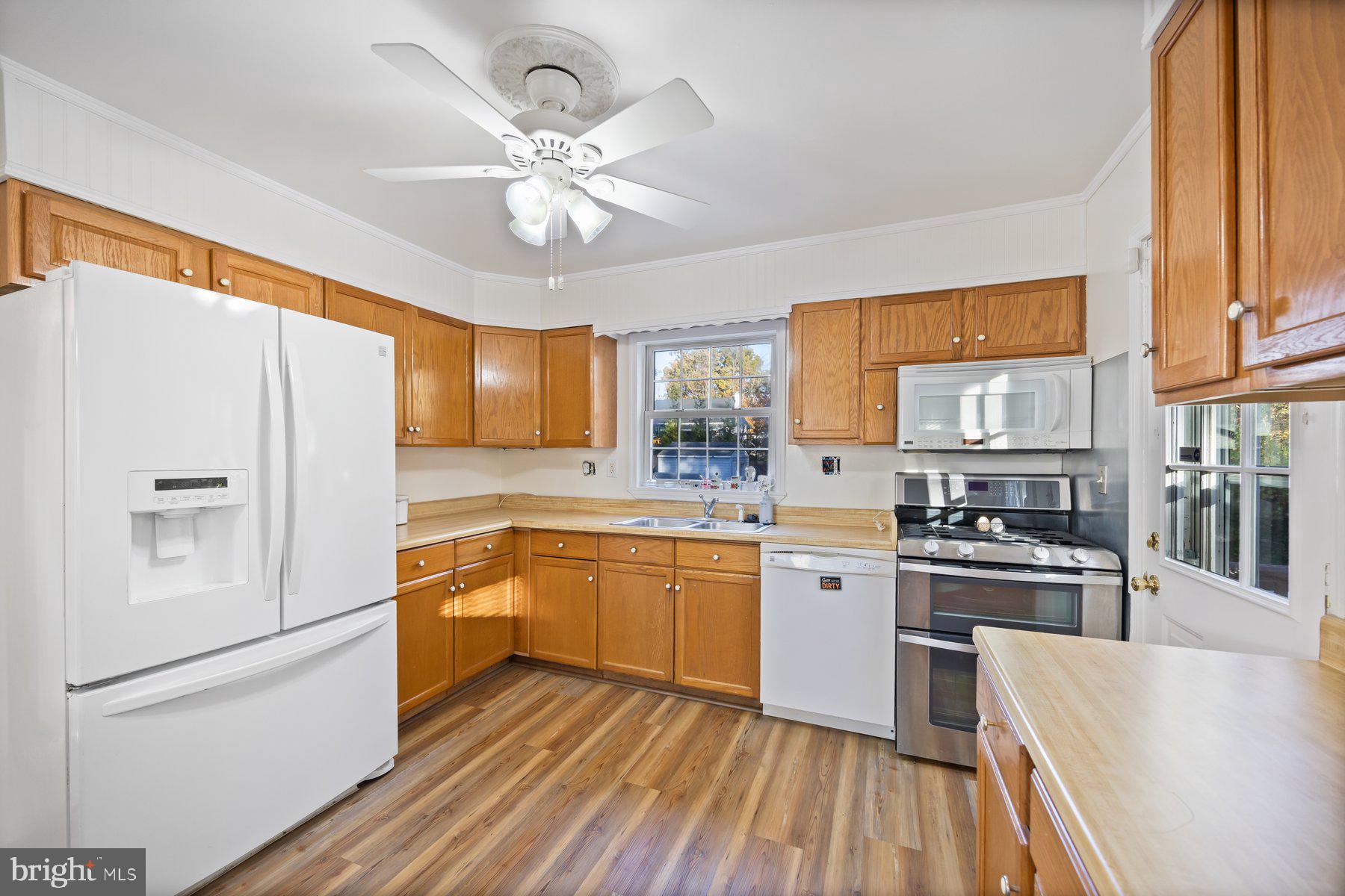 1003 Lee Road Glen Burnie, MD 21061 - Photo 6 of 44 a kitchen with a refrigerator a sink dishwasher a stove and white cabinets with wooden floor