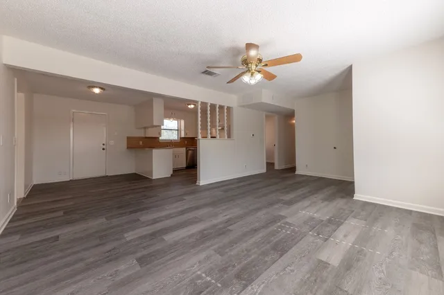 an empty room with wooden floor chandelier fan and windows