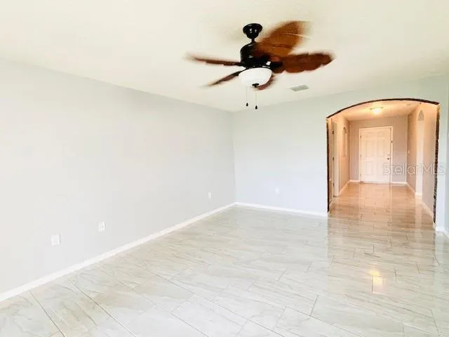 an empty room with a chandelier fan and wooden floor