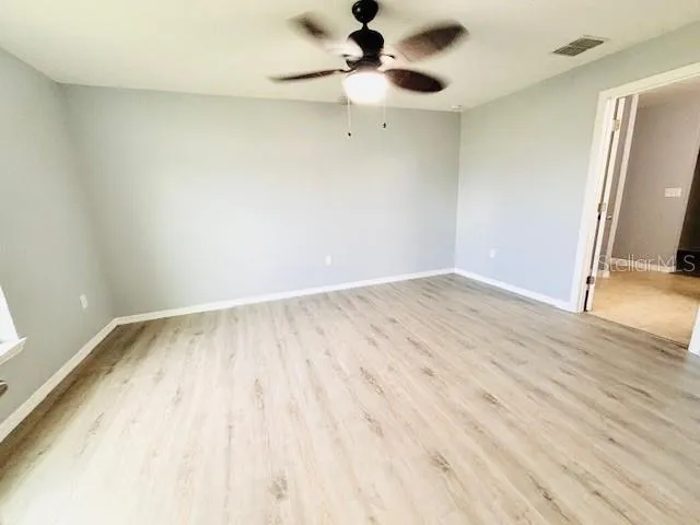 an empty room with wooden floor fan and windows