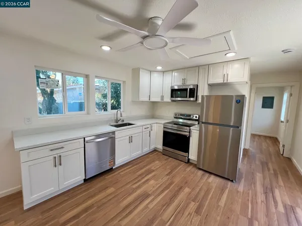 a kitchen with granite countertop a refrigerator a sink dishwasher a stove and white countertops with wooden floor