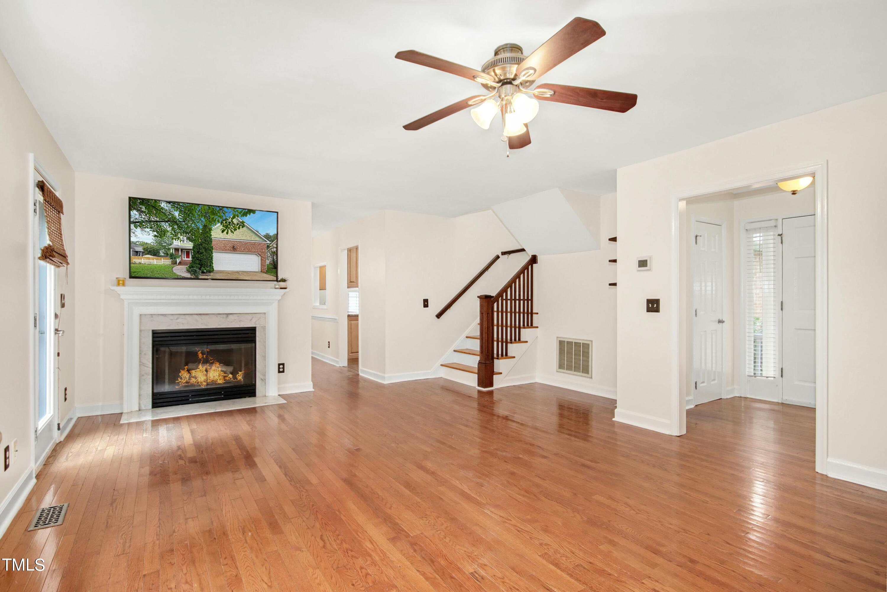 8605 Yucca Trail Raleigh, NC 27615 - Photo 5 of 42 an empty room with windows a fireplace a ceiling fan and wooden floor