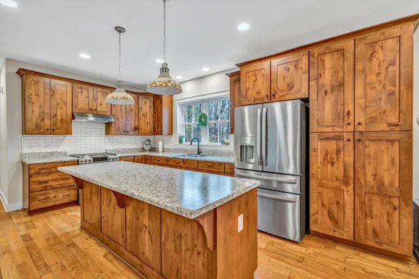 a kitchen with stainless steel appliances granite countertop a refrigerator a sink dishwasher and wooden cabinets with wooden floor