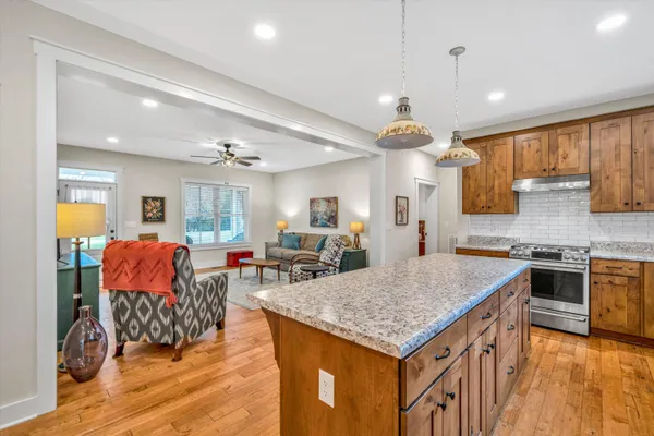 a kitchen with stainless steel appliances granite countertop a stove top oven a sink dishwasher and a dining table with wooden floor