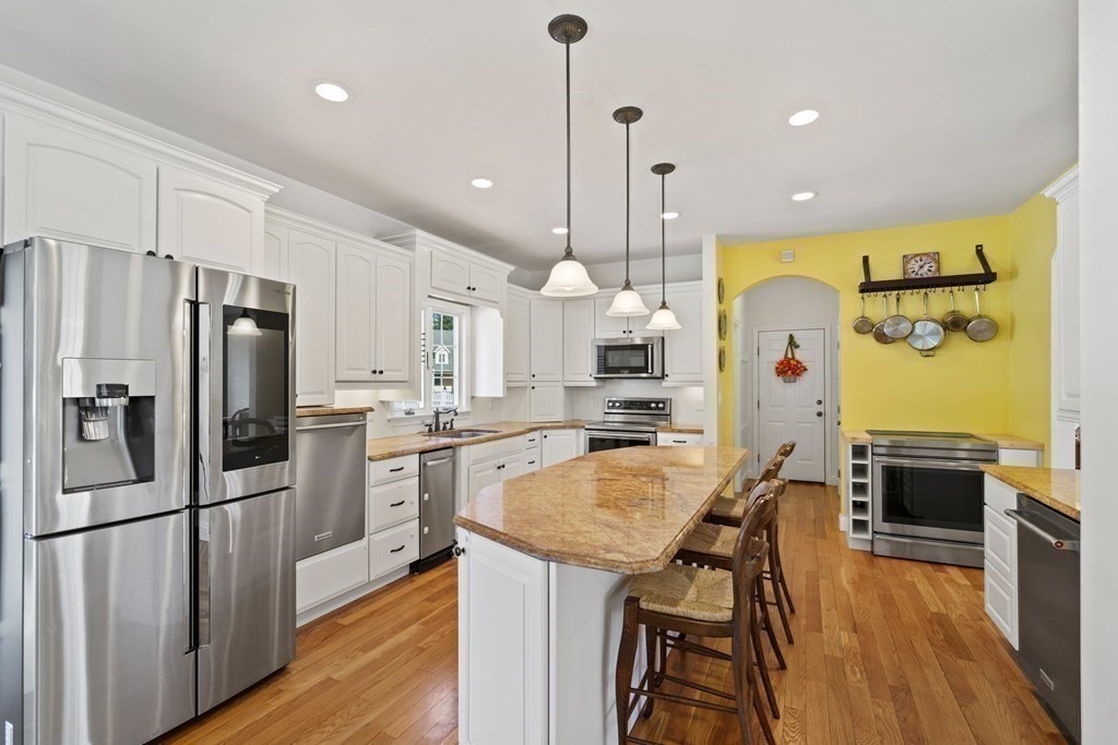 137 Randall Road Stow, MA 01775 - Photo 8 of 38 a kitchen with stainless steel appliances kitchen island granite countertop a refrigerator a stove a sink a dining table and chairs with wooden floor