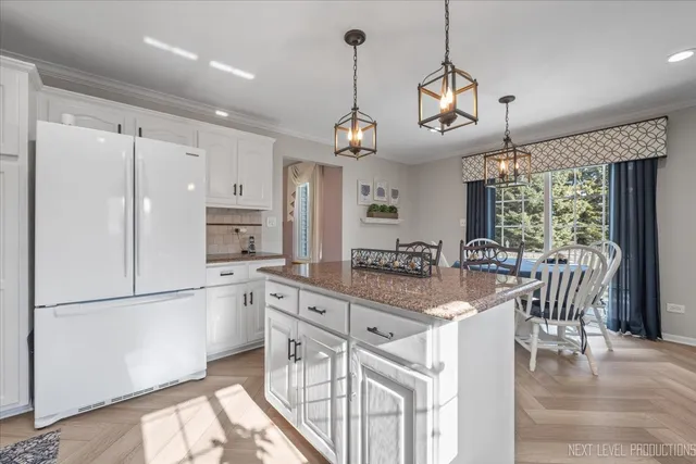 a kitchen with stainless steel appliances granite countertop a refrigerator a sink dishwasher a dining table and chairs with wooden floor