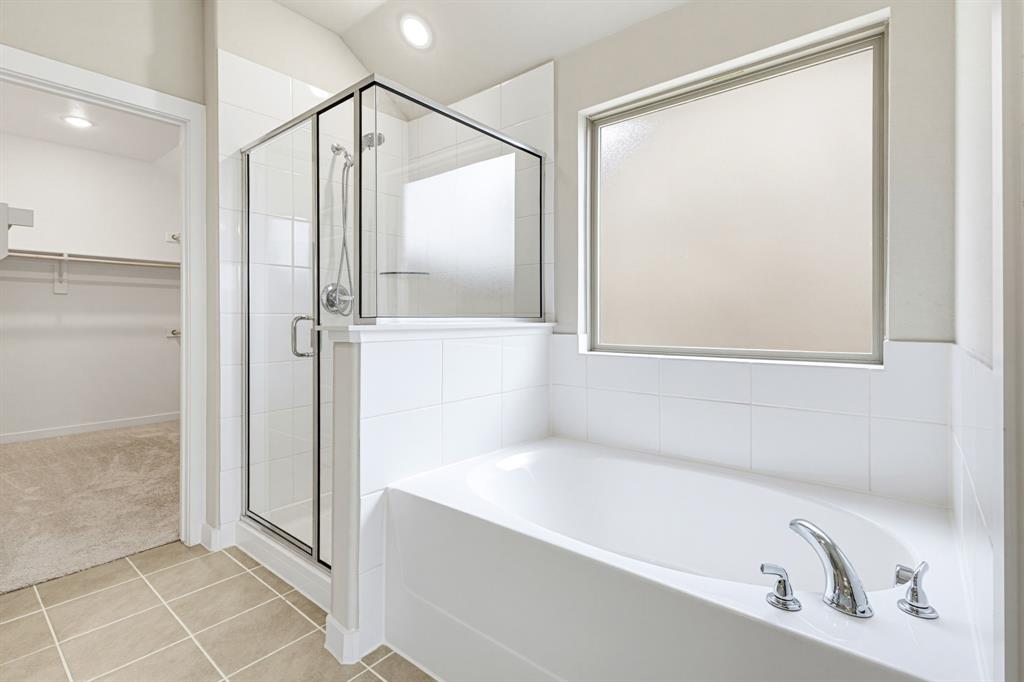 2108 Mossfield Lane Forney, TX 75126 - Photo 17 of 28 Spacious bathroom featuring a built-in soaking tub with chrome fixtures, a separate glass-enclosed shower, and a large privacy window