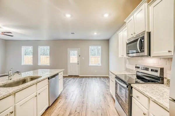 a kitchen with granite countertop a sink dishwasher stove and microwave with wooden floor