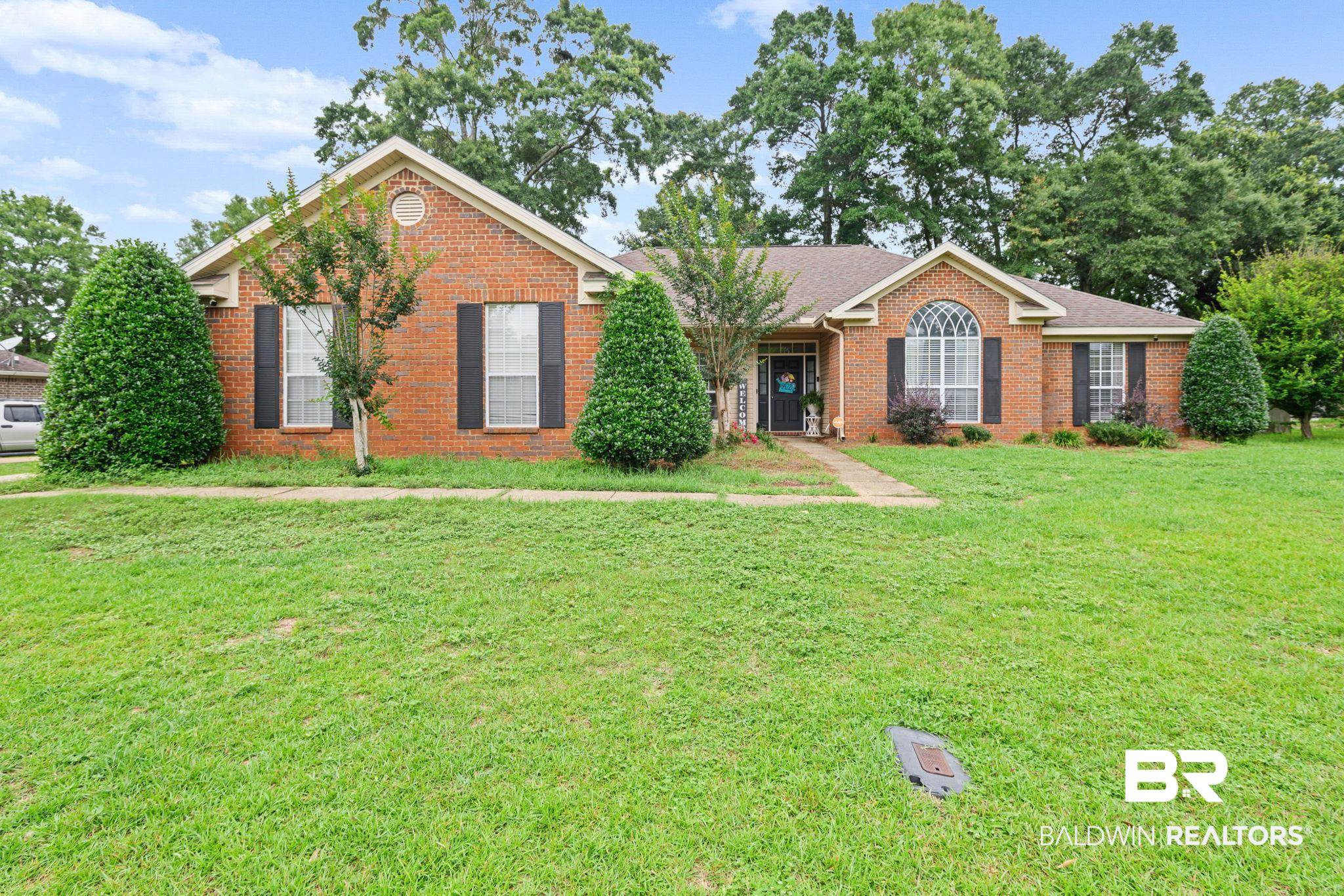 Brick exterior with an arched window, decorative shutters, and manicured shrubbery