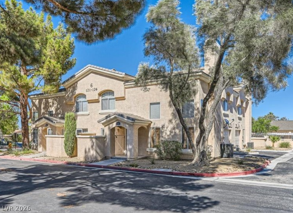 3950 South Sandhill Road, Unit 121 Las Vegas, NV 89121 - Photo 1 of 11 A cream-colored multi-level building is surrounded by well-maintained landscaping, featuring mature trees and a manicured stone bed.