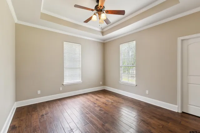 an empty room with wooden floor chandelier fan and windows