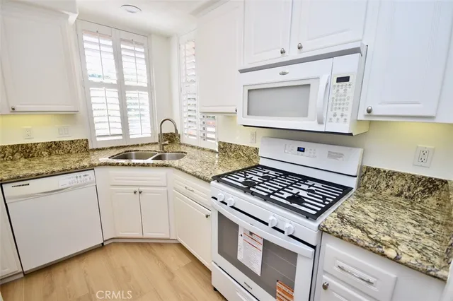 a kitchen with granite countertop a stove a sink and white cabinets