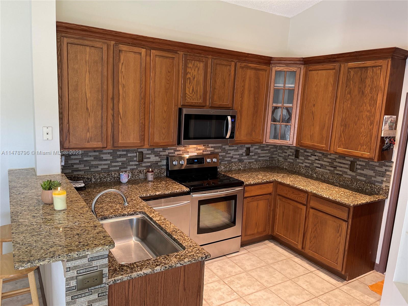 1135 Areca Way Weston, FL 33327 - Photo 12 of 45 a kitchen with granite countertop a sink wooden cabinets and stainless steel appliances