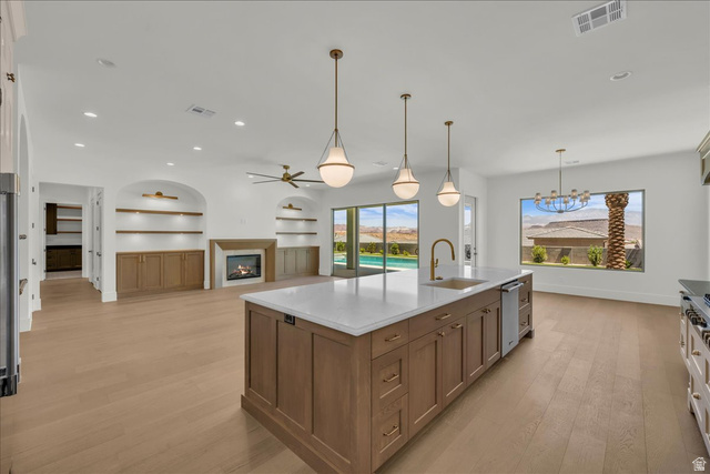 1620 Belayer Drive St. George, UT 84770 - Photo 13 of 51 Open-concept living space featuring a substantial kitchen island with a white countertop and undermount sink, light wood-finish flooring, a contemporary fireplace, built-in shelving with lower cabinetry, and large windows overlooking a pool and desert lan
