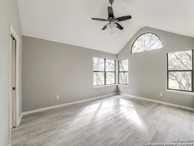 an empty room with wooden floor chandelier fan and windows