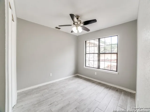 an empty room with wooden floor fan and windows
