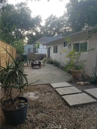 a view of a backyard with table and chairs potted plants and large tree