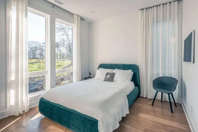 a large bed sitting in a bedroom next to a window with a chair and a lamp next to a window