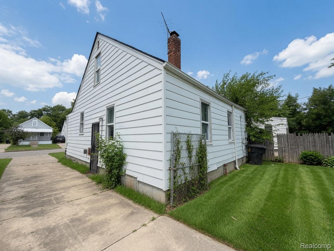7286 Faust Avenue Detroit, MI 48228 - Photo 3 of 19 White siding exterior with a pitched roof, brick chimney, concrete driveway, and a fenced yard