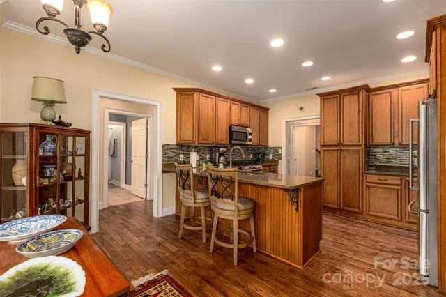 a kitchen with stainless steel appliances kitchen island granite countertop a refrigerator a stove a sink a dining table and chairs with wooden floor