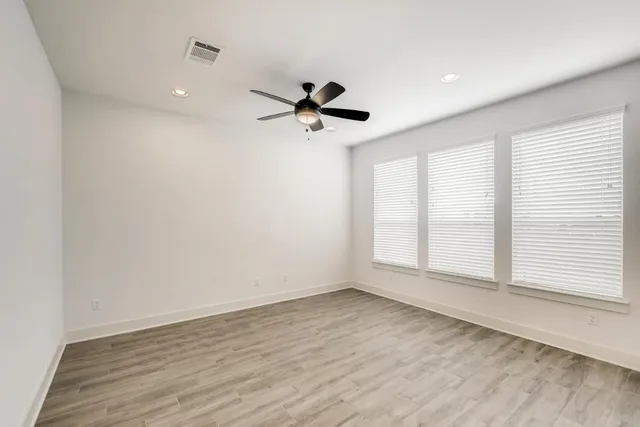 an empty room with wooden floor ceiling fan and windows