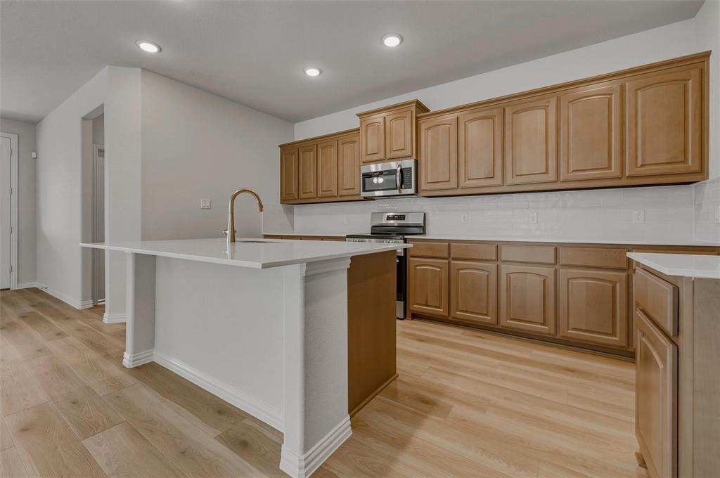 1337 Frio Drive Springtown, TX 76082 - Photo 11 of 40 Kitchen featuring wood-finish flooring, recessed lighting, a kitchen island with a white countertop and brass-finish faucet, extensive cabinetry, and stainless steel appliances