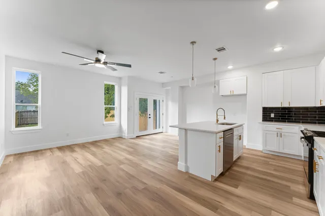 a kitchen with granite countertop a stove a sink and white cabinets with wooden floor