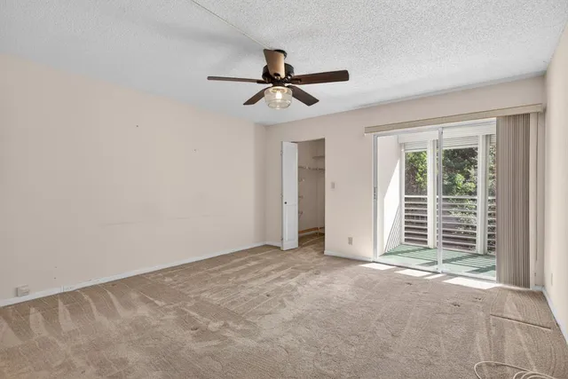 an empty room with chandelier fan and windows