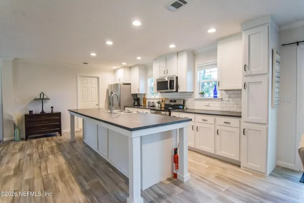a kitchen with kitchen island a sink a stove a refrigerator and white cabinets with wooden floor