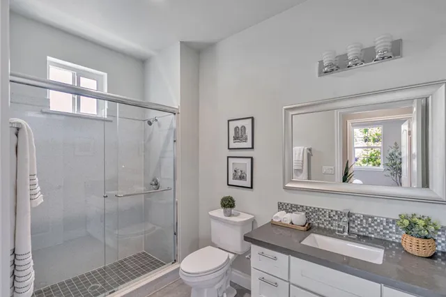 a bathroom with a granite countertop sink a toilet a mirror and shower
