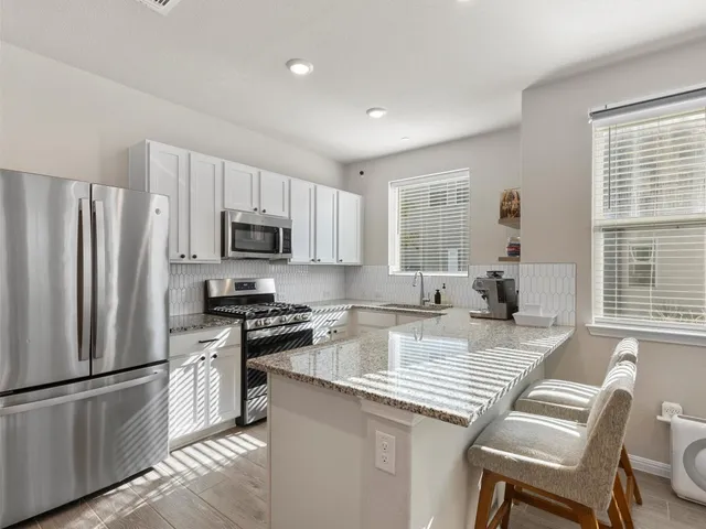 a kitchen with stainless steel appliances granite countertop a stove a sink a microwave a refrigerator and white cabinets