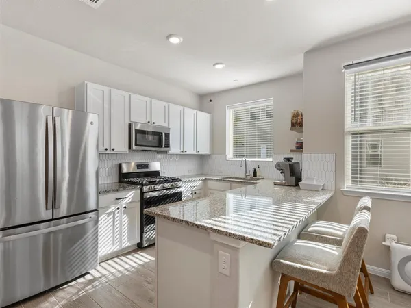 a kitchen with kitchen island granite countertop a stove a sink a refrigerator white cabinets and wooden floor
