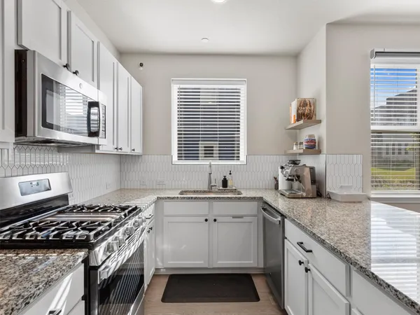 a kitchen with kitchen island granite countertop a stove top oven a sink dishwasher a refrigerator and white cabinets with wooden floor