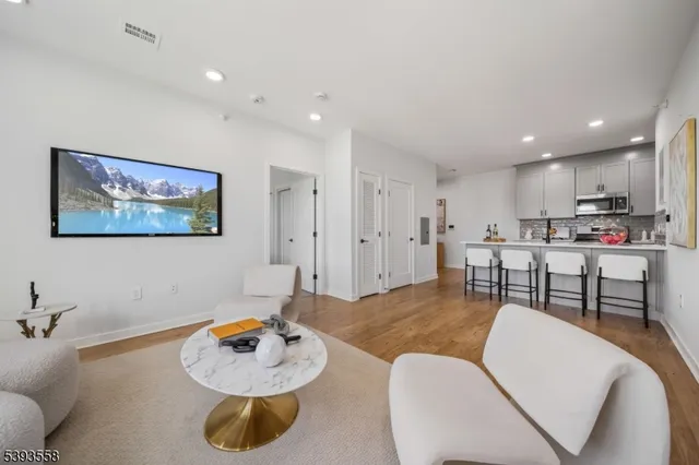 a living room with stainless steel appliances furniture a rug and a kitchen view