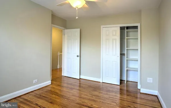 a view of an empty room with wooden floor and a ceiling fan