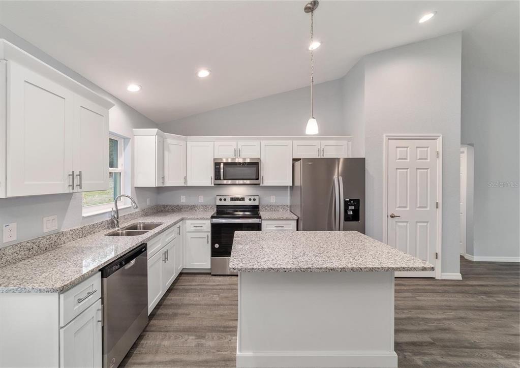15673 Southwest 37th Circle Ocala, FL 34473 - Photo 5 of 19 a large kitchen with stainless steel appliances kitchen island granite countertop a stove a sink dishwasher and a refrigerator with wooden floor