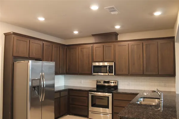 a kitchen with stainless steel appliances granite countertop a refrigerator a stove a sink and a microwave