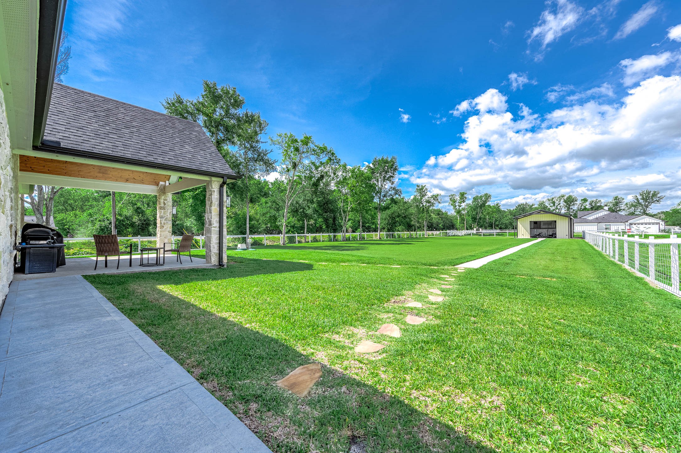 8032 Short Road Needville, TX 77461 - Photo 27 of 50 The backyard offers plenty of space to enjoy outdoor living, complete with a covered patio ideal for dining and entertaining. The expansive lawn extends to a large outbuilding that provides excellent potential for storage, a workshop, or additional utility space.