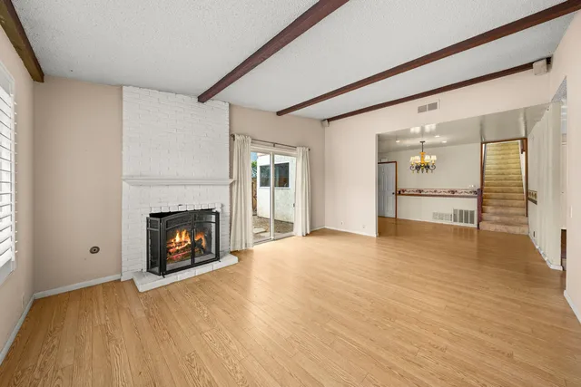 a view of an empty room with wooden floor fireplace and a window