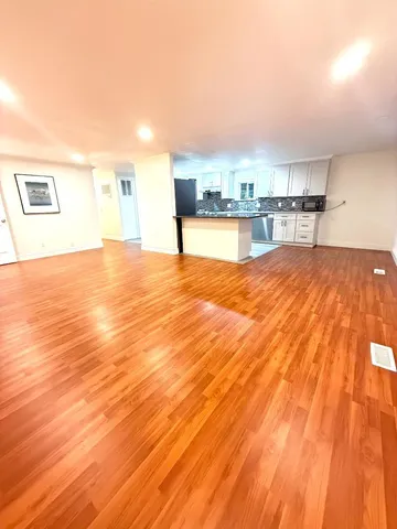 a view of kitchen and empty room with wooden floor