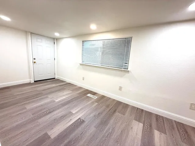 a view of an empty room with wooden floor and a window