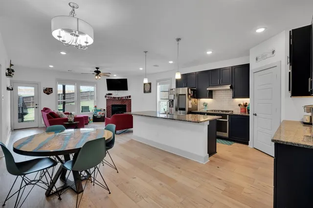 a kitchen with stainless steel appliances granite countertop a stove top oven a sink dishwasher a dining table and chairs with wooden floor