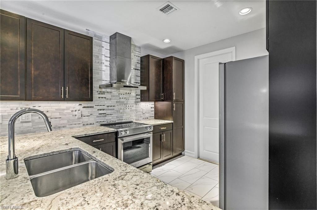 7841 Bristol Circle Naples, FL 34120 - Photo 7 of 31 Kitchen with stainless steel appliances, dark wood finish cabinets, light stone countertops, light marble finish floors, and tasteful backsplash