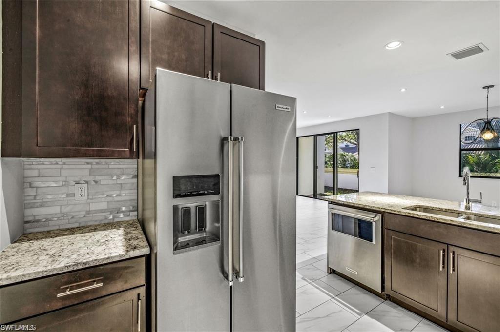 7841 Bristol Circle Naples, FL 34120 - Photo 9 of 31 Kitchen with stainless steel appliances, dark wood finish cabinetry, light stone counters, hanging light fixtures, and backsplash