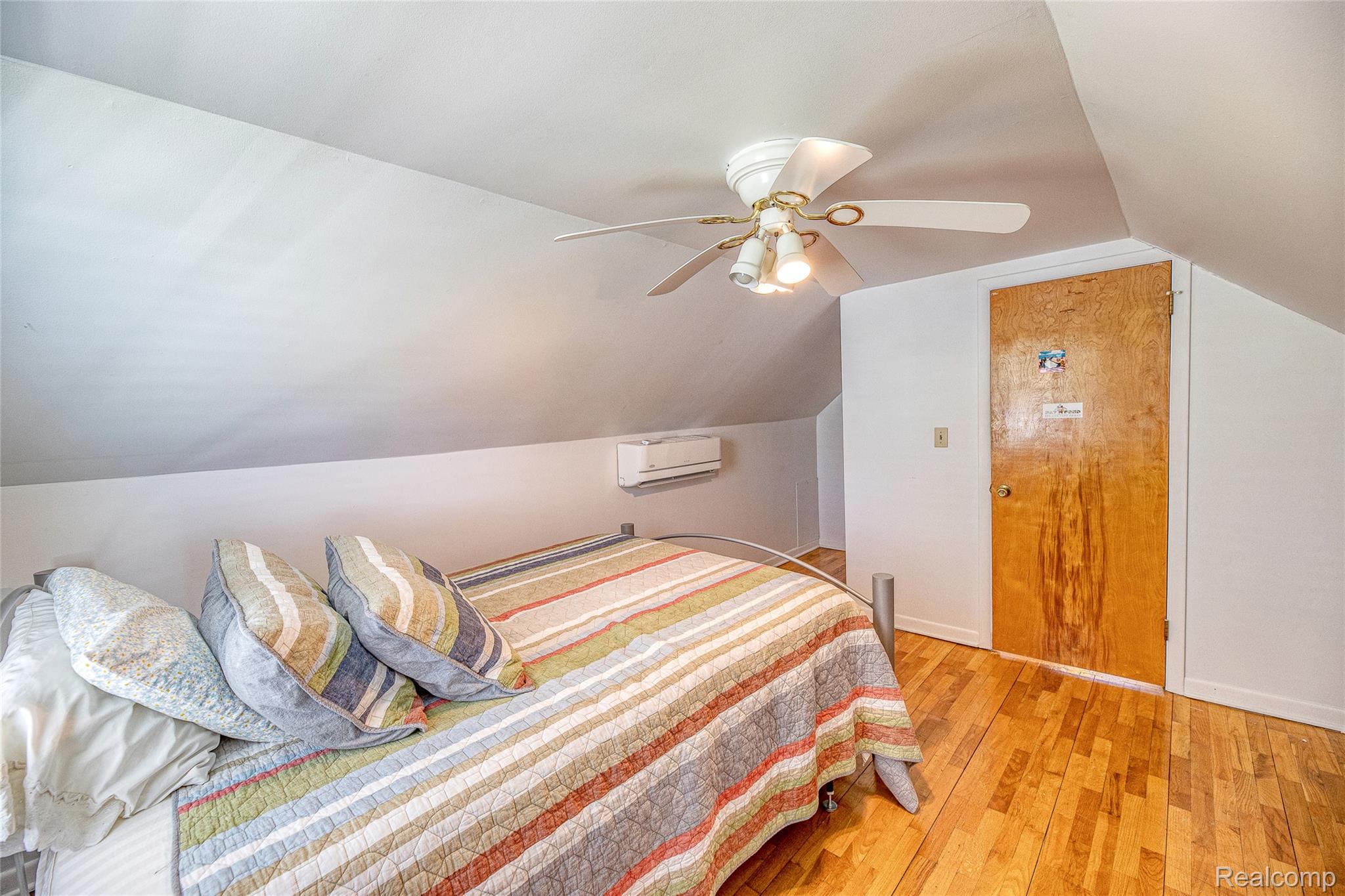 2855 Farmers Creek Road Metamora, MI 48455 - Photo 19 of 51 Sloped ceilings and wood-finish flooring characterize this room, featuring a built-in air conditioning unit, a ceiling fan with integrated lighting, and a solid wood door